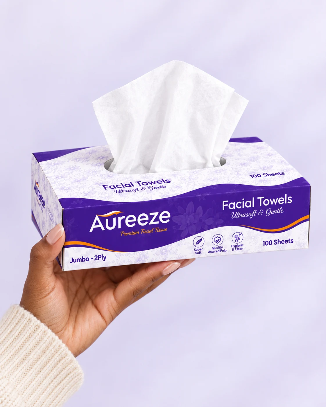 A hand in a cream knit sleeve holding up an Aureeze tissue box with a tissue rising from it, against a soft lavender background